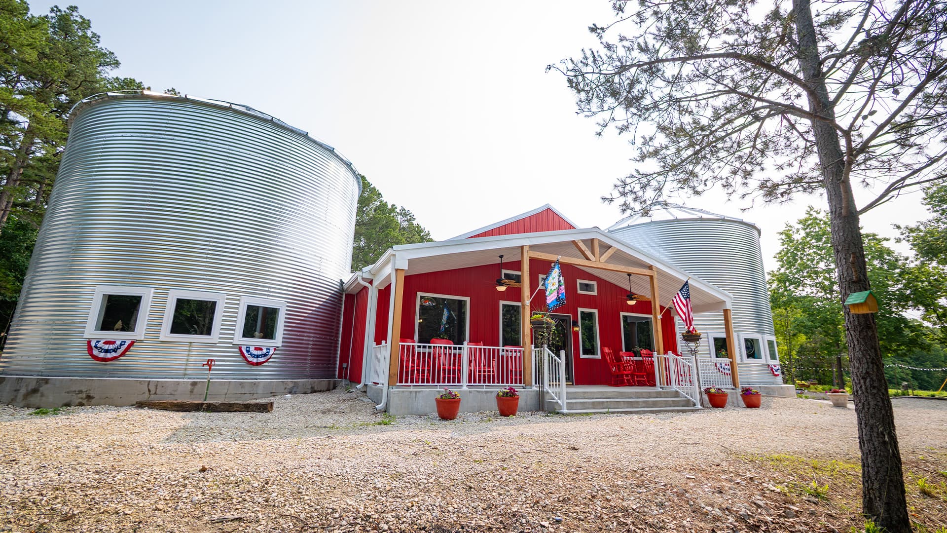 A red house with silver silos on either side, set in a wooded area.
