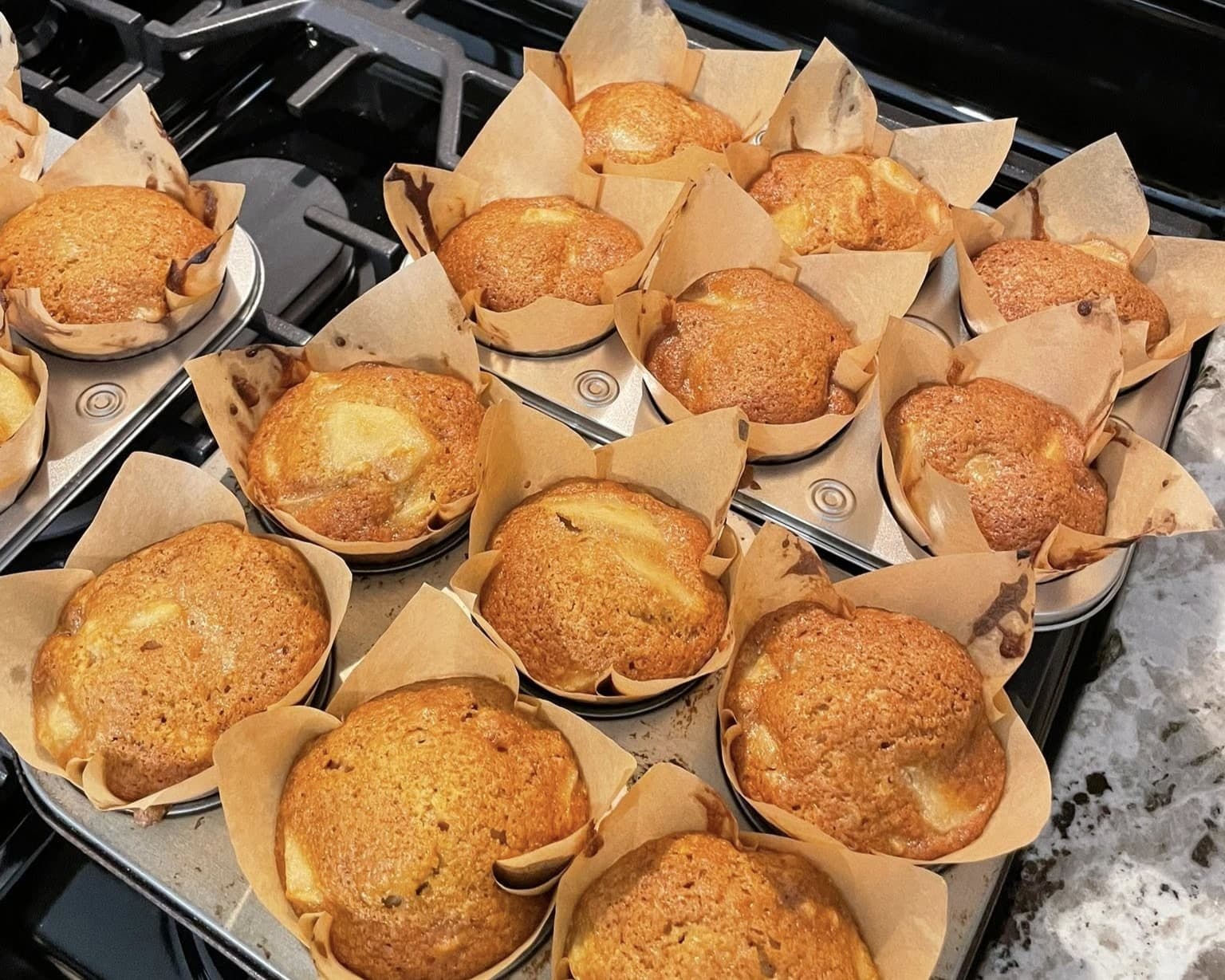 Baked muffins in brown paper liners cooling on a baking tray.